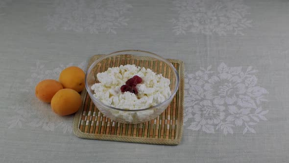 A Woman's Hand Throws Red Raspberries Into a Bowl of Cottage Cheese