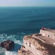 Aerial view of Nazare seascape, old Fortress and lighthouse on cliff; blue stormy water of Atlantic - VideoHive Item for Sale