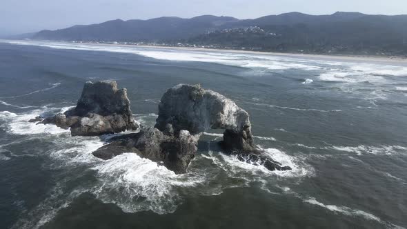Waves crash on the backside of Twin Rocks off the shore of Rockaway Beach, Oregon, aerial alt