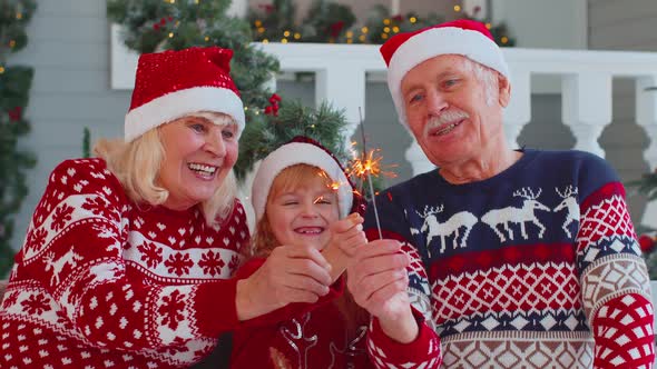 Happy Senior Couple Grandparents with Granddaughter Holding Lit Bengal Christmas Lights Sparklers alt