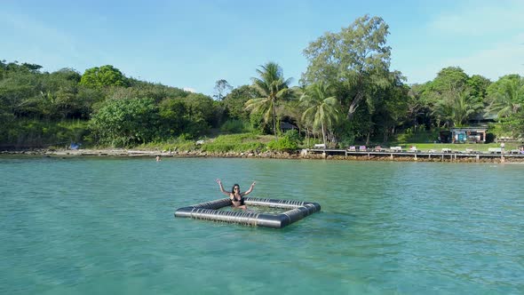 Girl sitting and waving in a inflatable floating device in the ocean, Koh Kood, Thailand alt