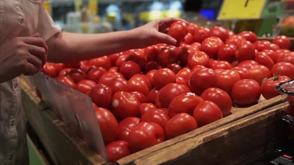 A female hand chooses red tomatoes at the market. 