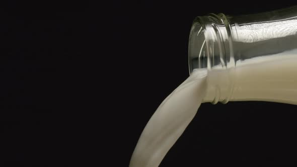  Milk flows from a neck of bottle on black backgrounds