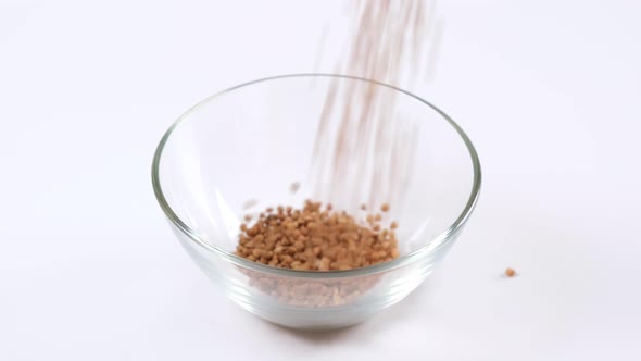 Raw dry buckwheat falling in a glass bowl on white background.