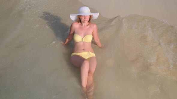 Woman in the Yellow Swim Suit and Hat Lies on the Beach at the Water of the Sea