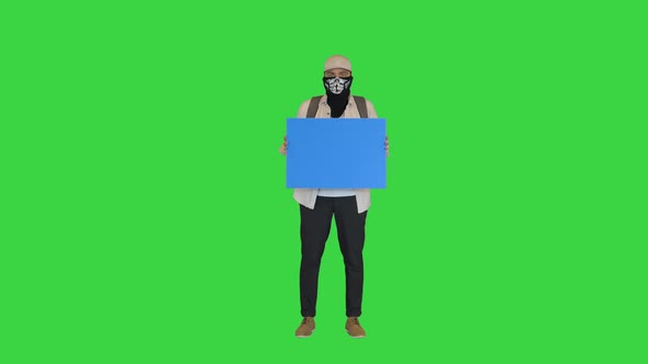 Young Man Protester with Covered Face Holding Blank Board on a Green Screen Chroma Key alt