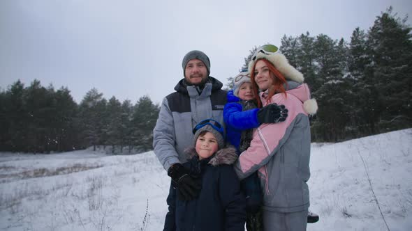 Portrait of a Happy Family with Cute Little Male Children in Winter Forest During a Snowfall Smiling