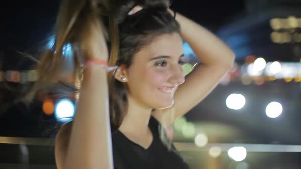 Teenage girl smiling and running hands through hair outdoors at night, portrait