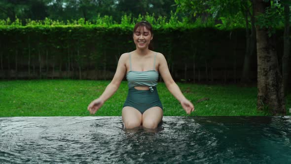 woman sitting on edge of swimming pool and playing water splashing