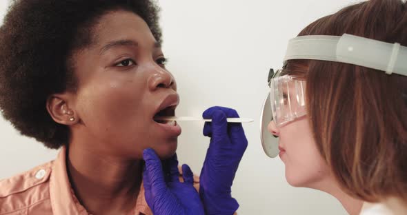 Otolaryngologist Examines A Female African American Throat With A Wooden Spatula alt