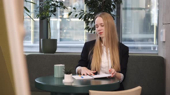 Young Woman Student Finishing Her Work with Notes and Papers in Cafe Restaurant