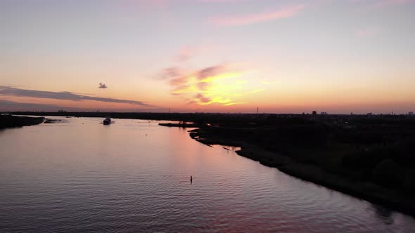 Colorful Sunset Sky With Silhouetted Barge Ship Sailing Across The River. - Wide Shot alt