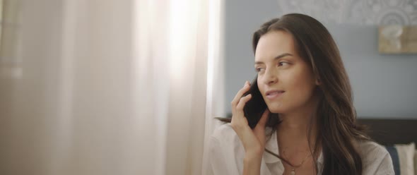 Close up of a woman talking to someone on the phone, near the window alt
