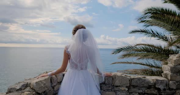 Back view of bride in dress looking at the sea in Montenegro from the fortress alt