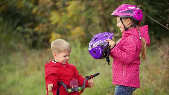 The little girl wears a protective helmet to her younger brother. he resists and does not want