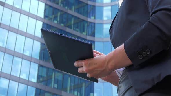 A Businesswoman Works on a Tablet - Closeup From Below - an Office Building in the Blurry Background alt