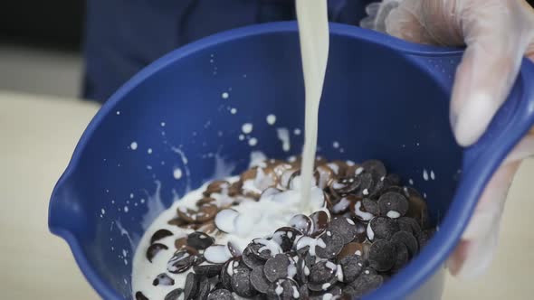 Pastry Chef Pouring White Cream Into a Blue Bowl with Chocolate Buttons