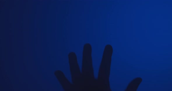 Silhouette of a man's hand banging against a window