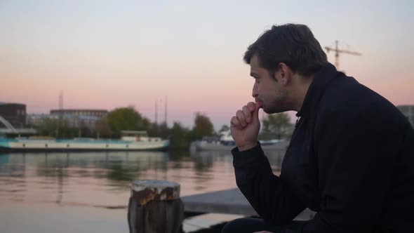 Wide shot of a young man snacking on an orange slice and smiling on a water pier during sunset alt