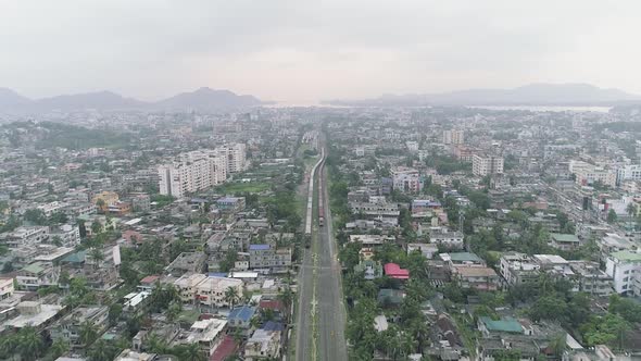 Long train passing through Indian city with low buildings on a dusty sky early morning alt
