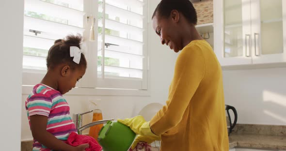 Happy african american mother and daughter washing dishes in kitchen alt