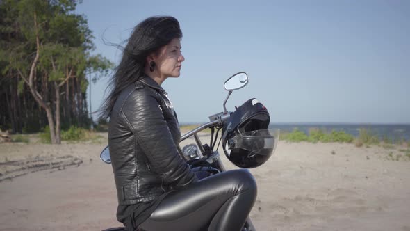 Side View of the Girl Sitting on the Motorcycle Looking Away on the Riverbank alt