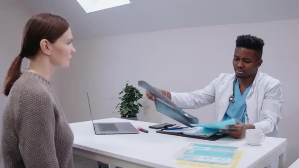 Doctor Gives Consultation to a Patient Looking at Xrays Wearing Medical Gown alt