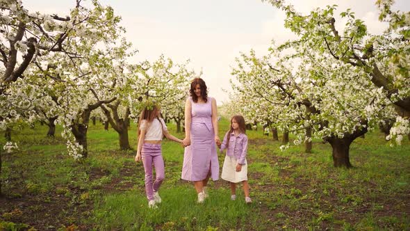 Mom Walks with Her Two Daughters in the Garden Among the Flowering Trees alt