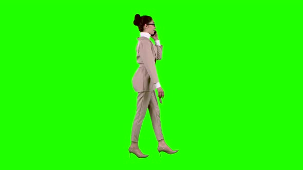 Woman Is Walking and Talking on the Phone. Green Screen. Side View. Slow Motion alt