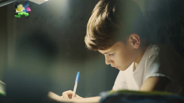 Young Male Child is Very Concentrated Doing His Homework at Desk in His Room alt
