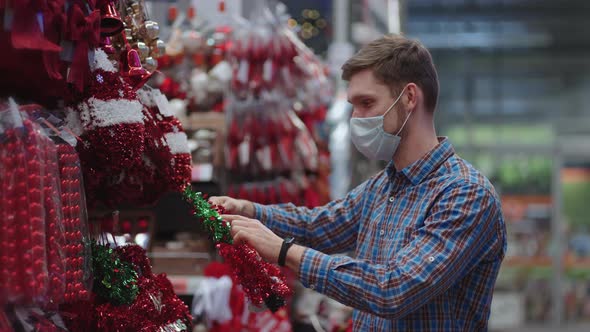 A Man in a Protective Mask in a Jewelry Store and Garlands with Toys for Christmas Trees and at Home alt