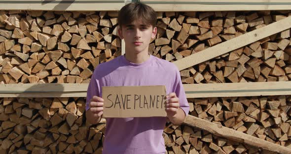 Outdoor of Men Activist with Save the Planet Ecology Poster. In Background Chopped Trees alt