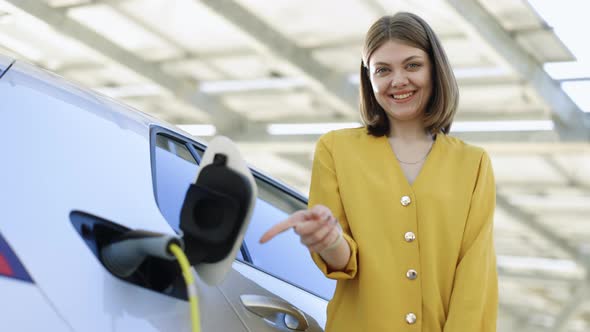 Woman Standing on Charging Station Looking at Camera and Showing Thumb Up