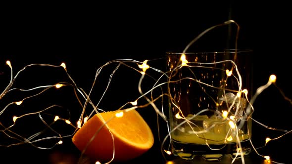 A Slice Of Orange And A Glass With Ice In Which Juice Is Poured With A New Years Garland
