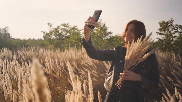Attractive Fun Stylish Redhead Woman in the Field at Sunset Making a Selfie with a Bouquet of