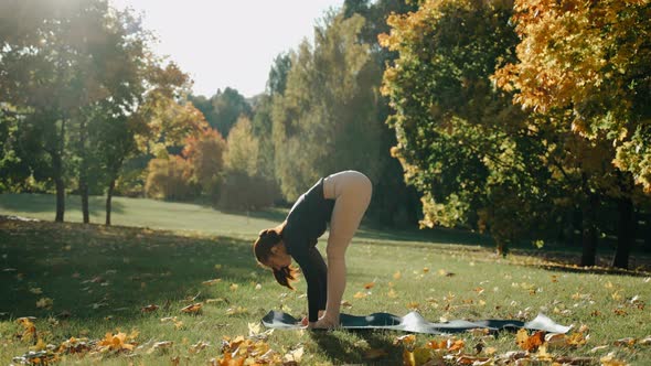 Young Woman Doing Forward Bend and Chaturanga in Autumn City Park on a Yoga Mat