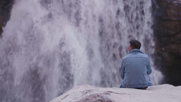 Young Indian Man sitting on rock and confidently looking at waterfall