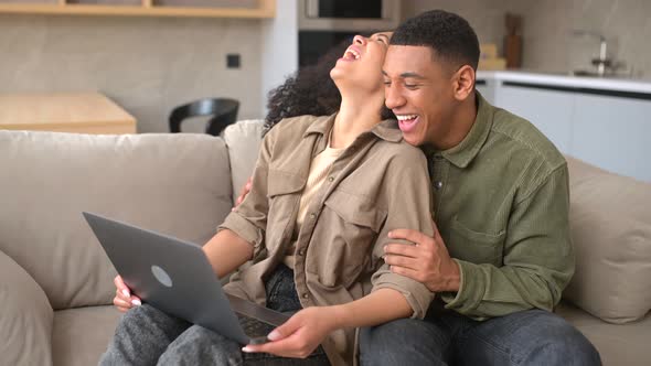 Overjoyed Multiracial Couple in Love Spending Leisure Time Online with a Laptop at Home