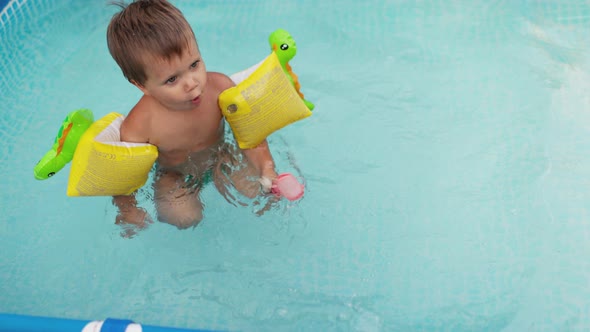 Kid in Oversleeves Swims in the Pool in the Yard alt