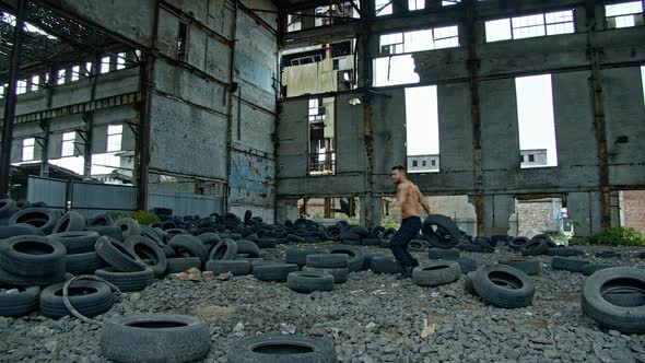 Strong man training workout. Muscular fitness shirtless man throwing tire outdoor alt