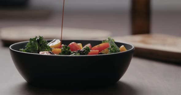 Slow Motion Pour Balsamic Sauce Over Salad with Kale and Cherry Tomatoes in Black Bowl on Concrete alt