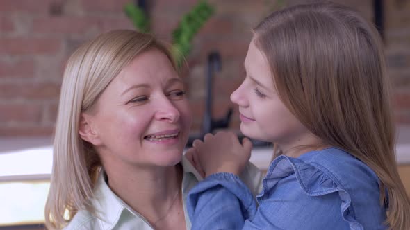 Happy Motherhood, Little Smiling Child Girl Tells Beloved Mum Whispering Secrets in Ear at Home alt