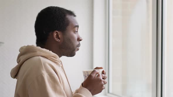 Unhappy Young Man With Mental Health Issues Standing In Kitchen At Home With Hot Drink