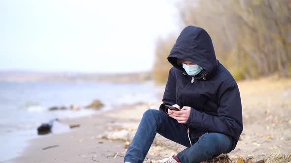 Teen Playing Online Video Games Sitting on Autumn Empty Beach During Pandemic Coronavirus Season
