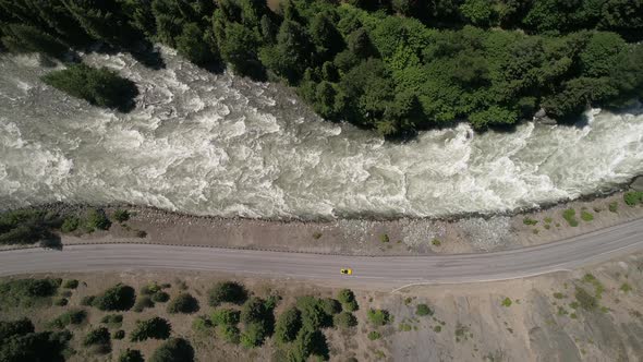 Overhead Horizontal Aerial Of Cars Driving In Nature On Mountain Highway By Raging River alt
