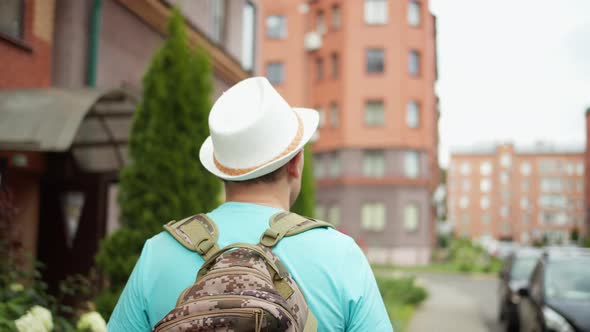 Man tourist in a hat and with a backpack travels through the city streets, camera tracking alt