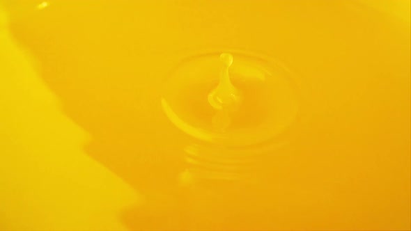A drop of orange juice falls on the surface of the juice. Slow motion. alt