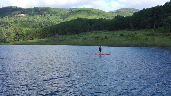 Aerial drone view of man is paddling on stand up paddleboarding in the mountain lake alt