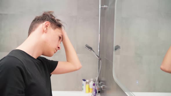 Hearingimpaired Young Man in Hearing Aids in the Bathroom Looks at Himself in the Mirror alt