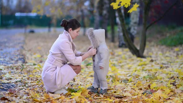 mother carefully fastens clothes to her baby daughter on the street in the autumn evening alt